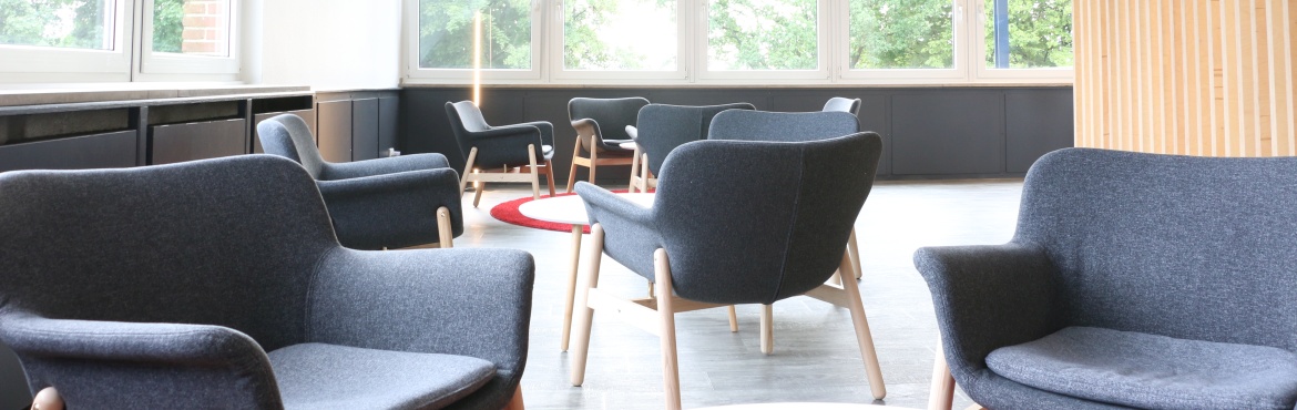 Blick in die Lounge der Cantina mit acht grauen Sesseln und einem runden weiß roten Teppich