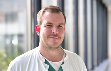 Nick Fröhlke im weißen Kittel in einem Flur des Krankenhauses