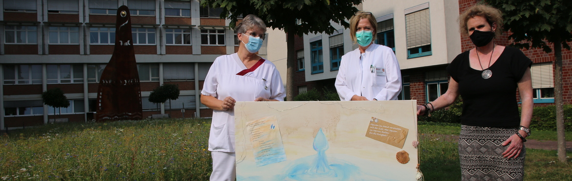 Schwester, Chefärztin und Spenderin stehen mit dem Bild im Skulpturgarten des Rhein-Maas Klinikums