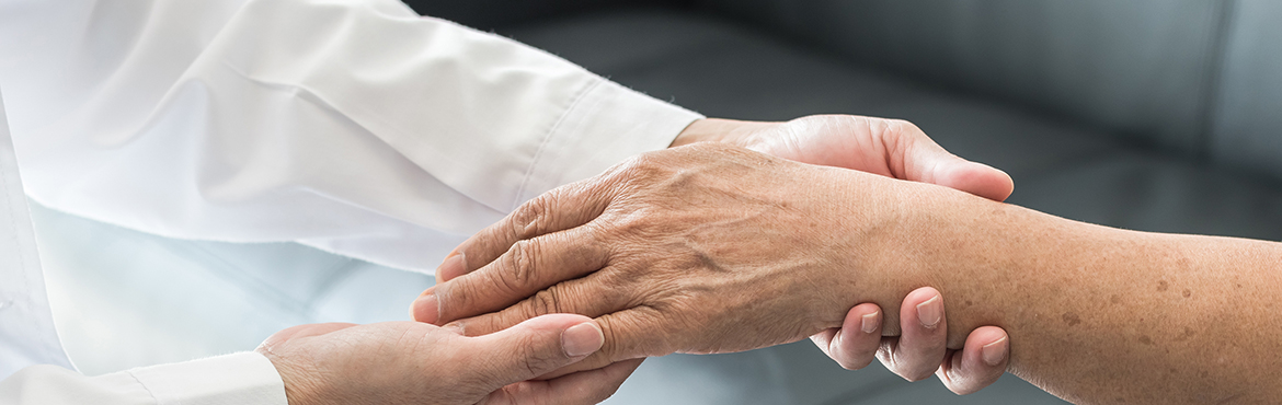 Die Hände eines Arztes halten die Hand eines älteren Patienten.